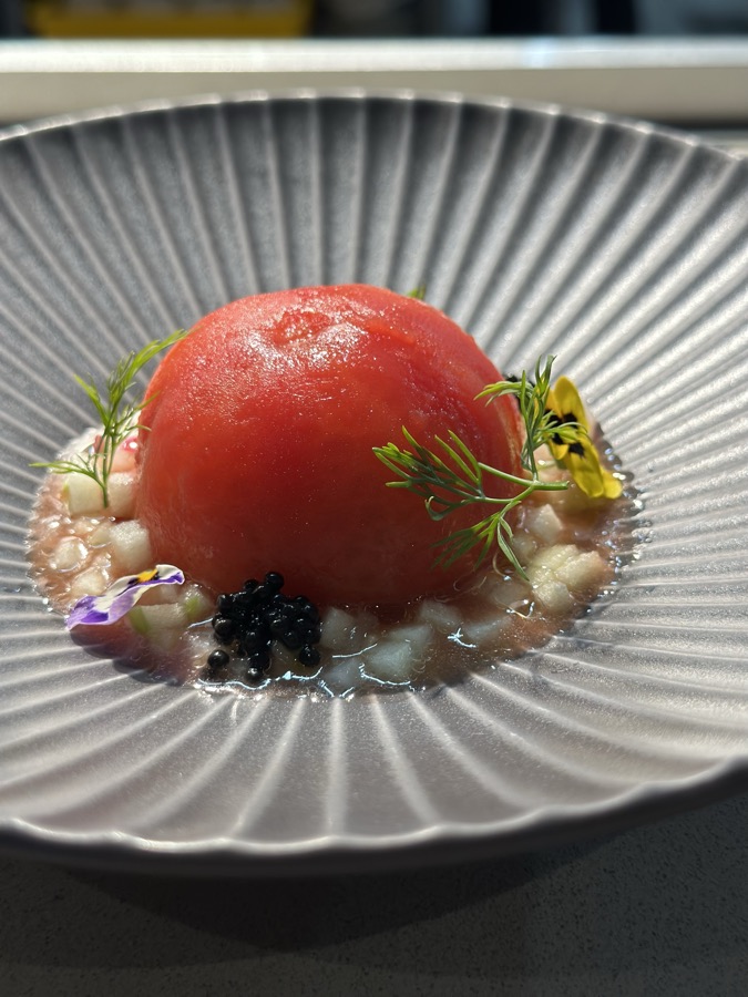 A ripe tomato set in a ribbed bowl with caviar, herbs and edible flowers