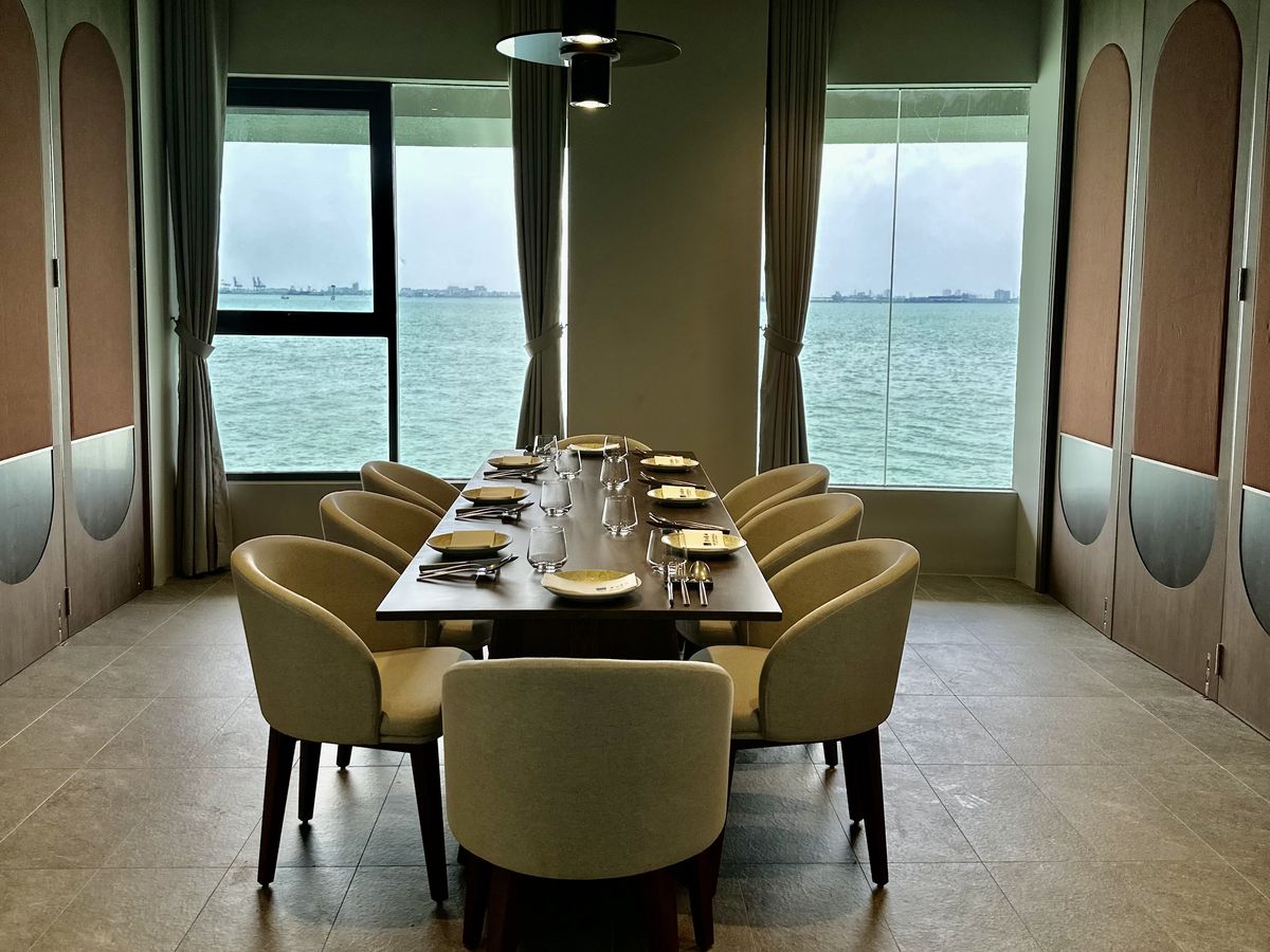 A long table set for eight between two tall sea-view windows in a private room