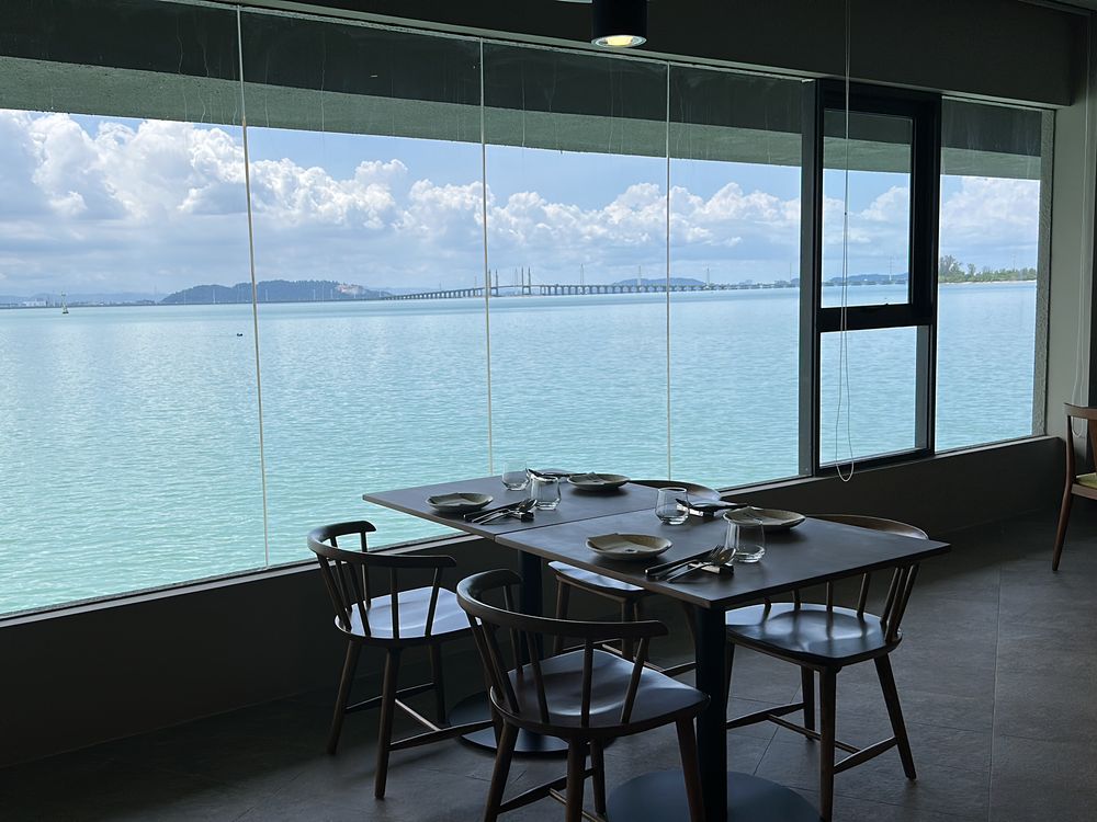 A table set for two beside a floor-to-ceiling window over calm turquoise water